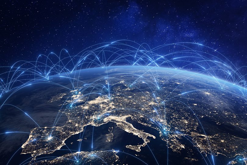 View of Earth at night from space, focused on Europe, with glowing city lights and digital blue lines illustrating global communication and data connections across countries.