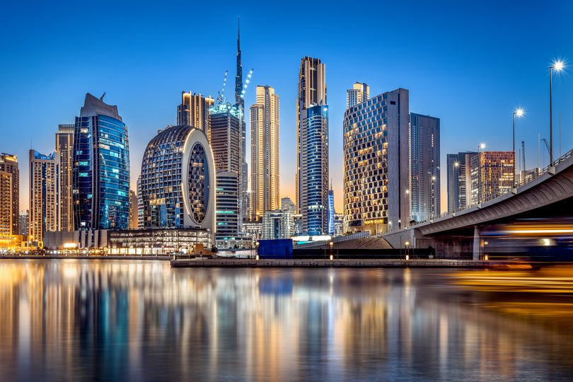 A twilight view of the Dubai skyline, featuring modern skyscrapers reflecting on calm waterfront.