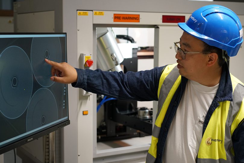 Researcher Wenjia Du is using the fast X-ray tomography to inspect the internal defects in a battery module. He is pointing at a screen showing images of a battery cell and highlighting areas of defect.