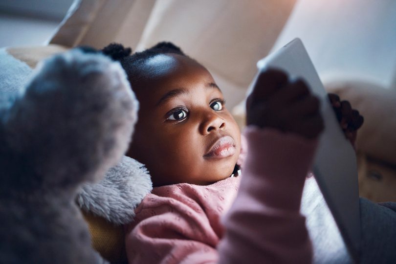Young black girl laying down looking at a digital device